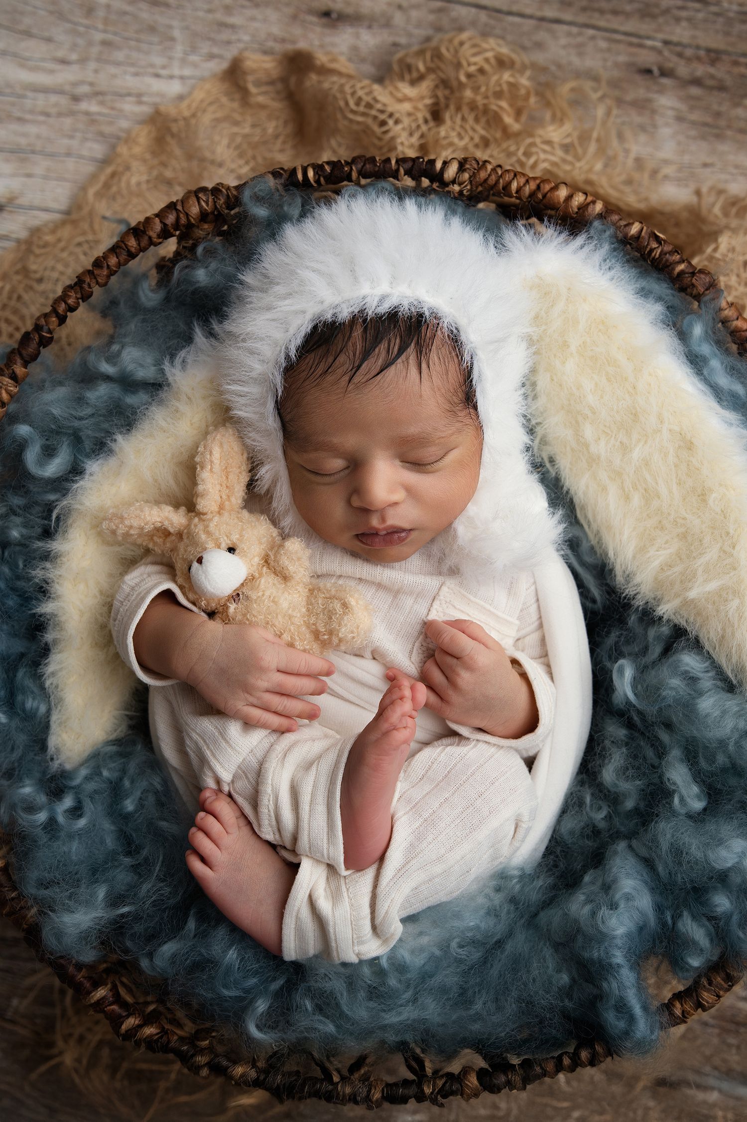Sleeping newborn in white outfit holding bunny toy on textured backdrop.
