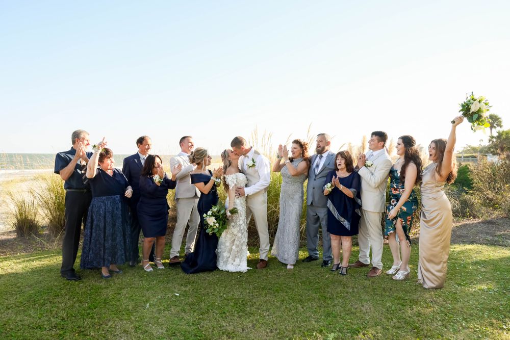 Wedding party poses for a group photo on a grassy lawn overlooking the water.