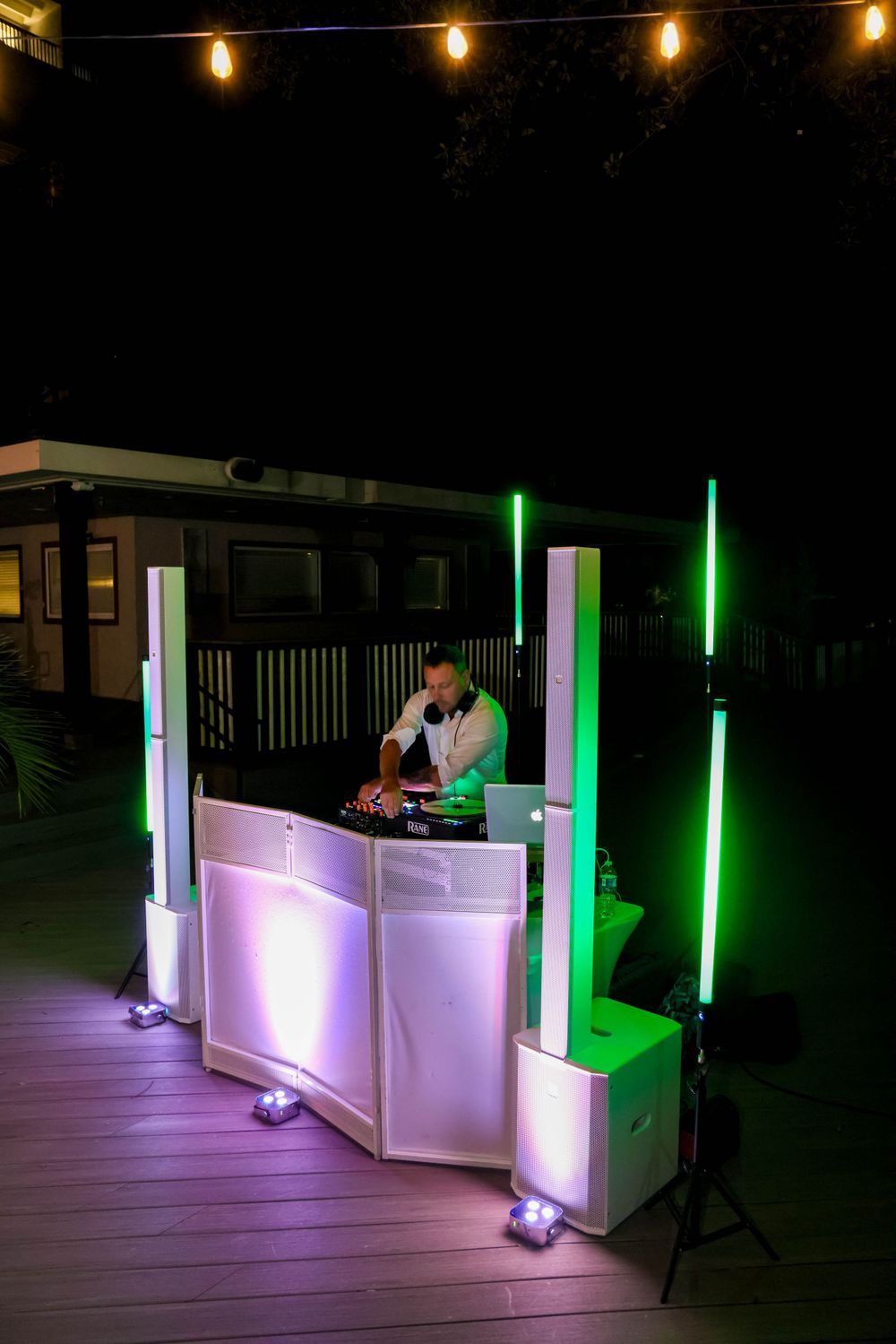 DJ booth with neon lighting setup on wooden deck at nighttime reception.
