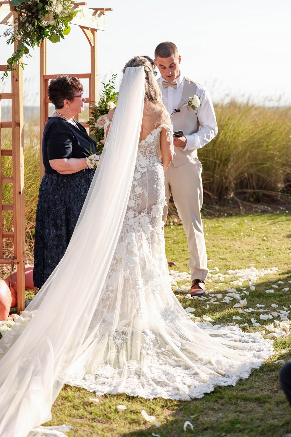 Wedding ceremony under wooden arch decorated with greenery and flowers.