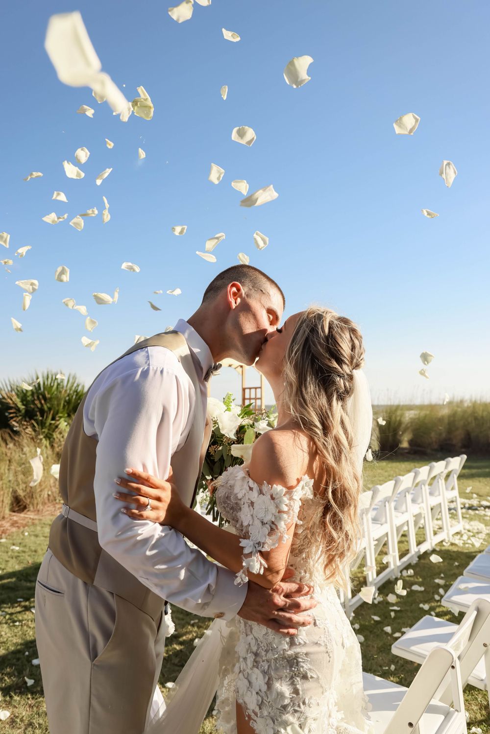 Newlyweds share romantic moment as rose petals float in breeze during outdoor ceremony.