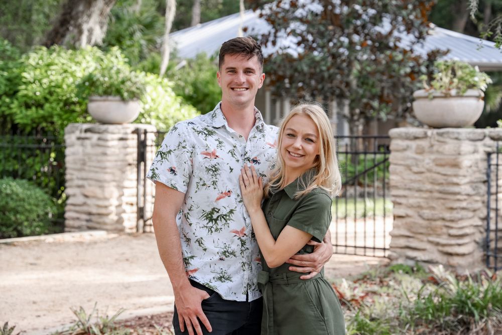 Casual couple in coordinated outfits poses by ornate garden gate.