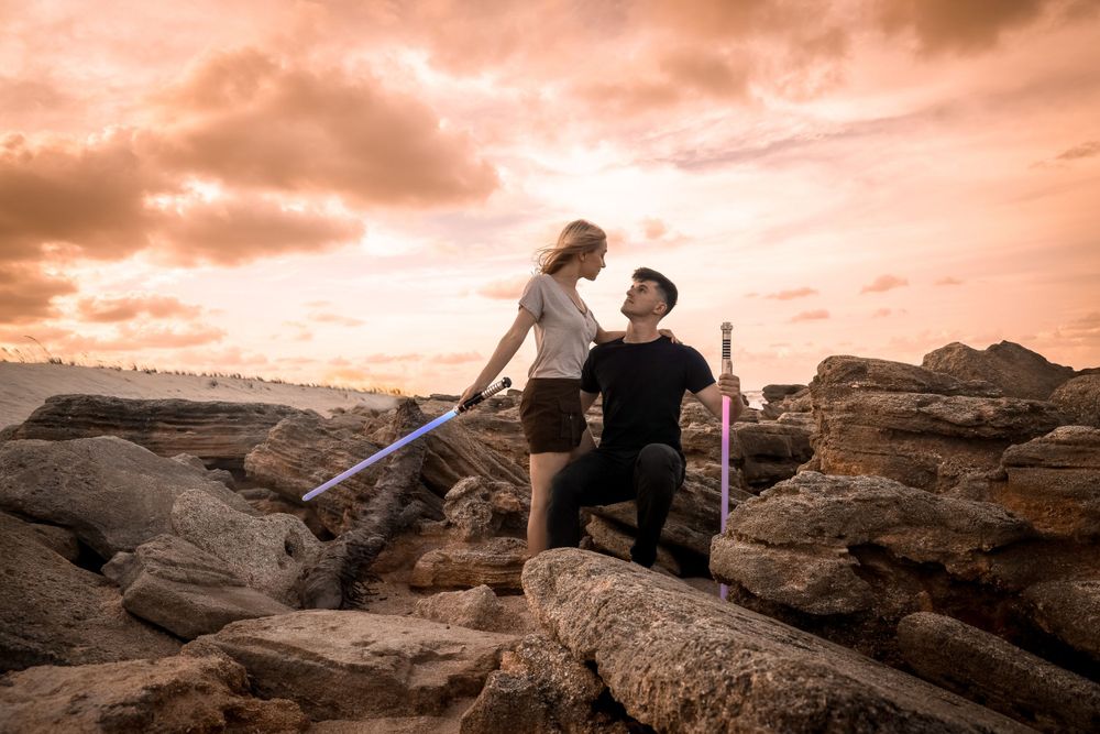 A romantic couples proposal holding lightsabers on rocky terrain at sunset.
