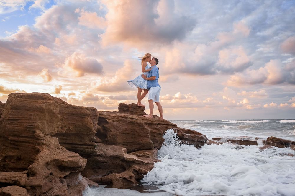 A couple enjoying a dramatic moment on oceanside cliffs with crashing waves.