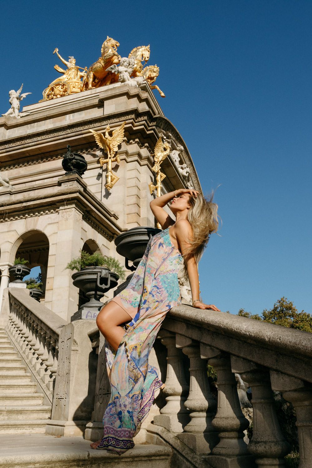 A person in a floral dress poses dramatically on ornate stone architecture.