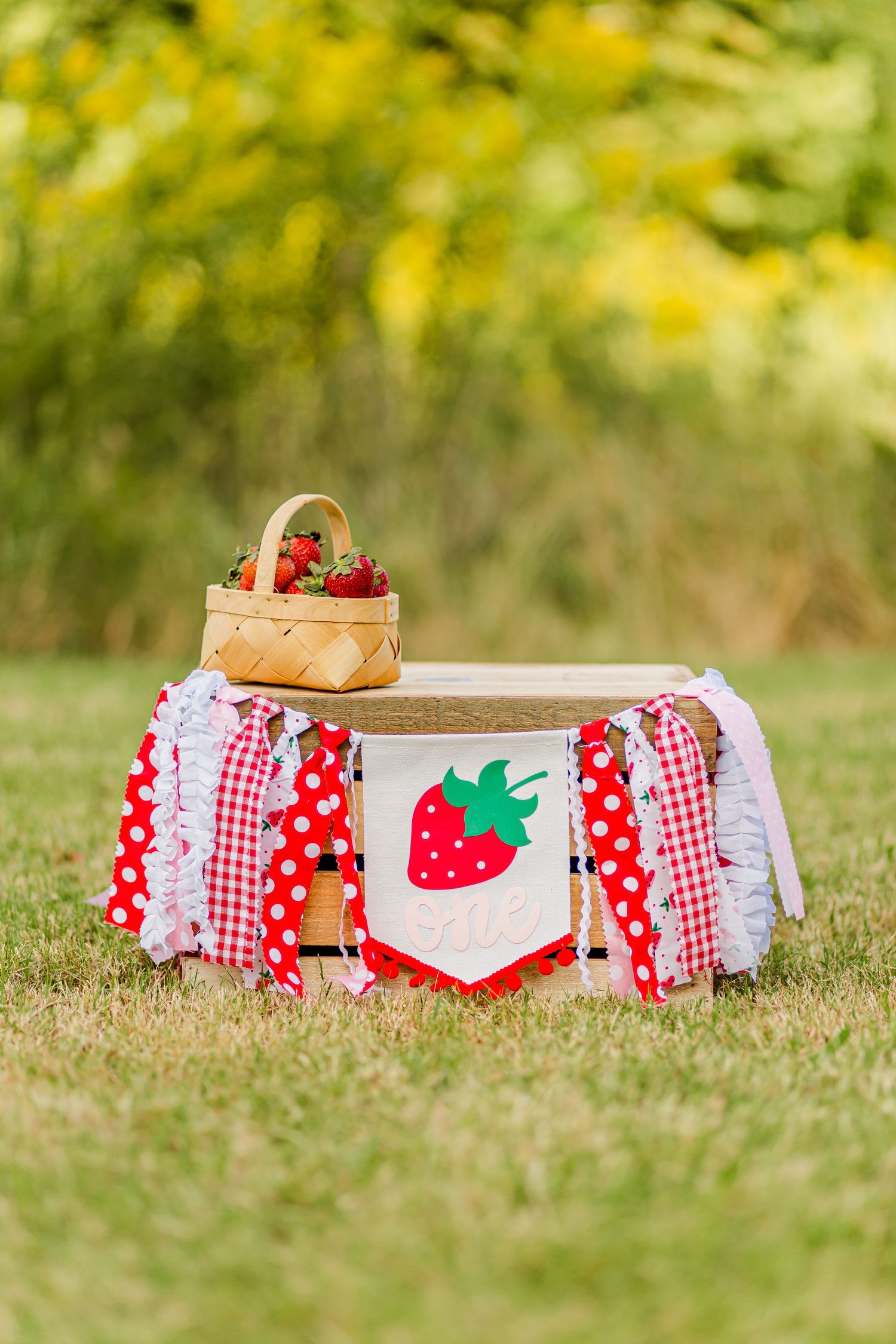 Strawberry-themed display with fabric banner and basket on wooden surface outdoors.