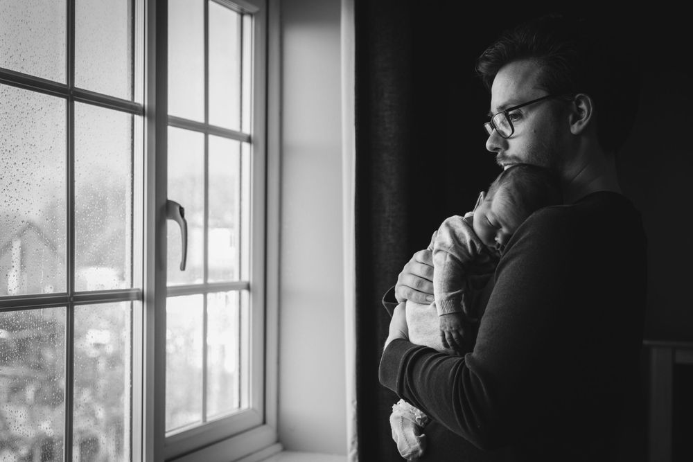 Silhouette of parent holding infant while looking out bright window.