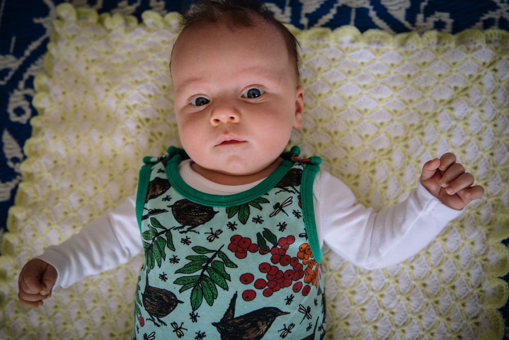 Baby wearing floral print outfit lying on patterned blanket.