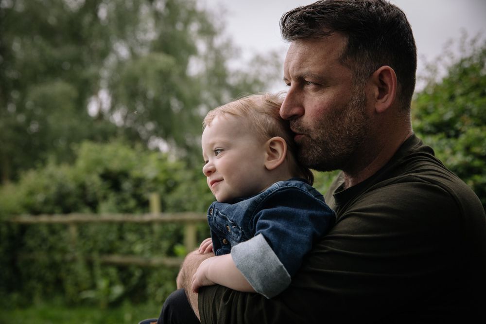 A tender outdoor moment between parent and child against a green natural background.