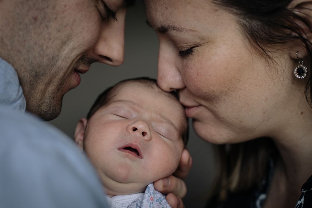 An intimate family moment with a sleeping infant being gently embraced by loving parents.