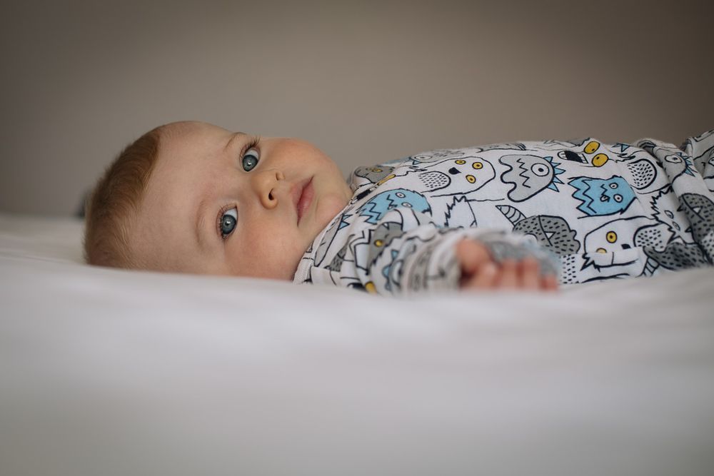 Close-up of an infant with bright eyes lying on white bedding wearing patterned clothing.