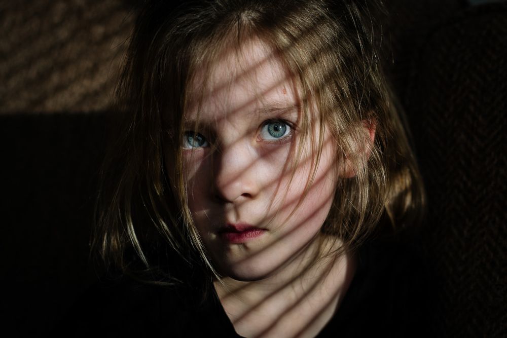Artistic portrait with shadows cast across a face, creating a dramatic effect in low light.