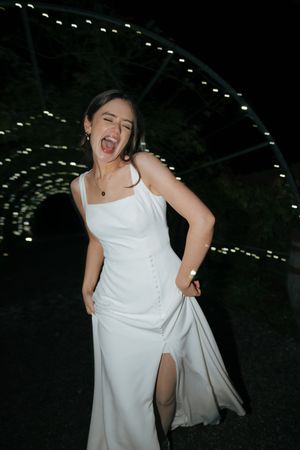 Joyful bride in sleek white dress dancing at nighttime wedding reception.
