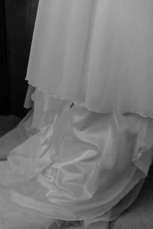 Black and white detail shot of flowing white wedding dress train on floor.