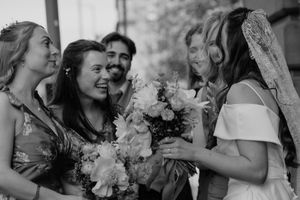 Black and white photo of a smiling bride in veil holding bouquet with bridesmaids and guests at wedding.
