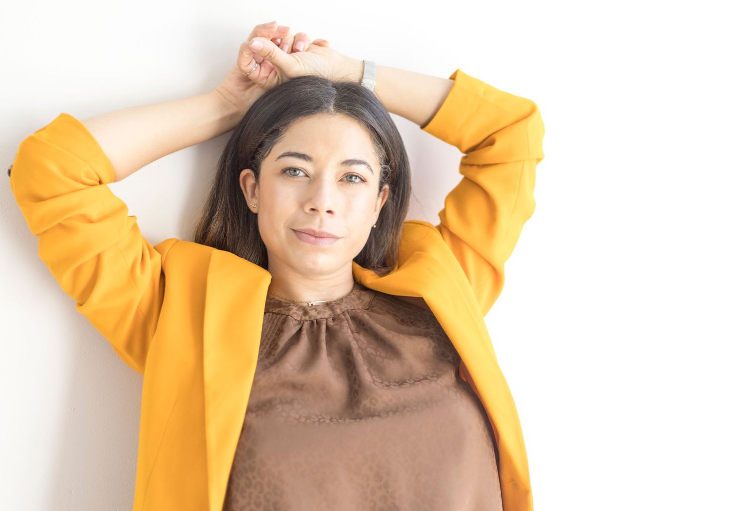 Casual pose in vibrant yellow blazer and brown blouse against white backdrop.