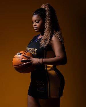 Basketball player in Lakers jersey poses against brown backdrop holding ball in promotional style portrait.
