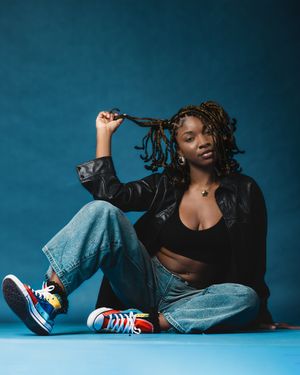 Casual fashion portrait featuring denim, sneakers and relaxed pose on blue backdrop.
