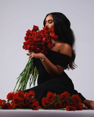 Beautiful artistic portrait of someone in black dress holding red roses against light gray backdrop, creating striking contrast.