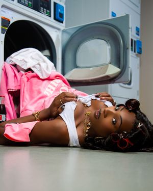 Person in pink and white clothing lying on floor in laundromat with washing machines visible in background.