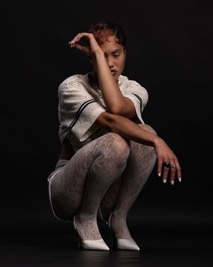 Artistic portrait of a figure crouching in white textured clothing against a dark background.