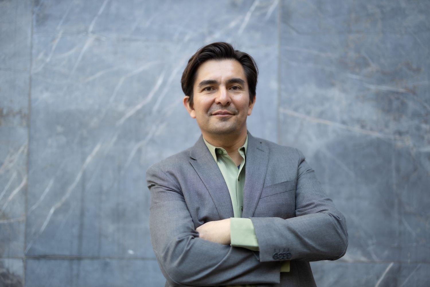 Confident businessman in gray suit and mint green shirt poses with crossed arms.