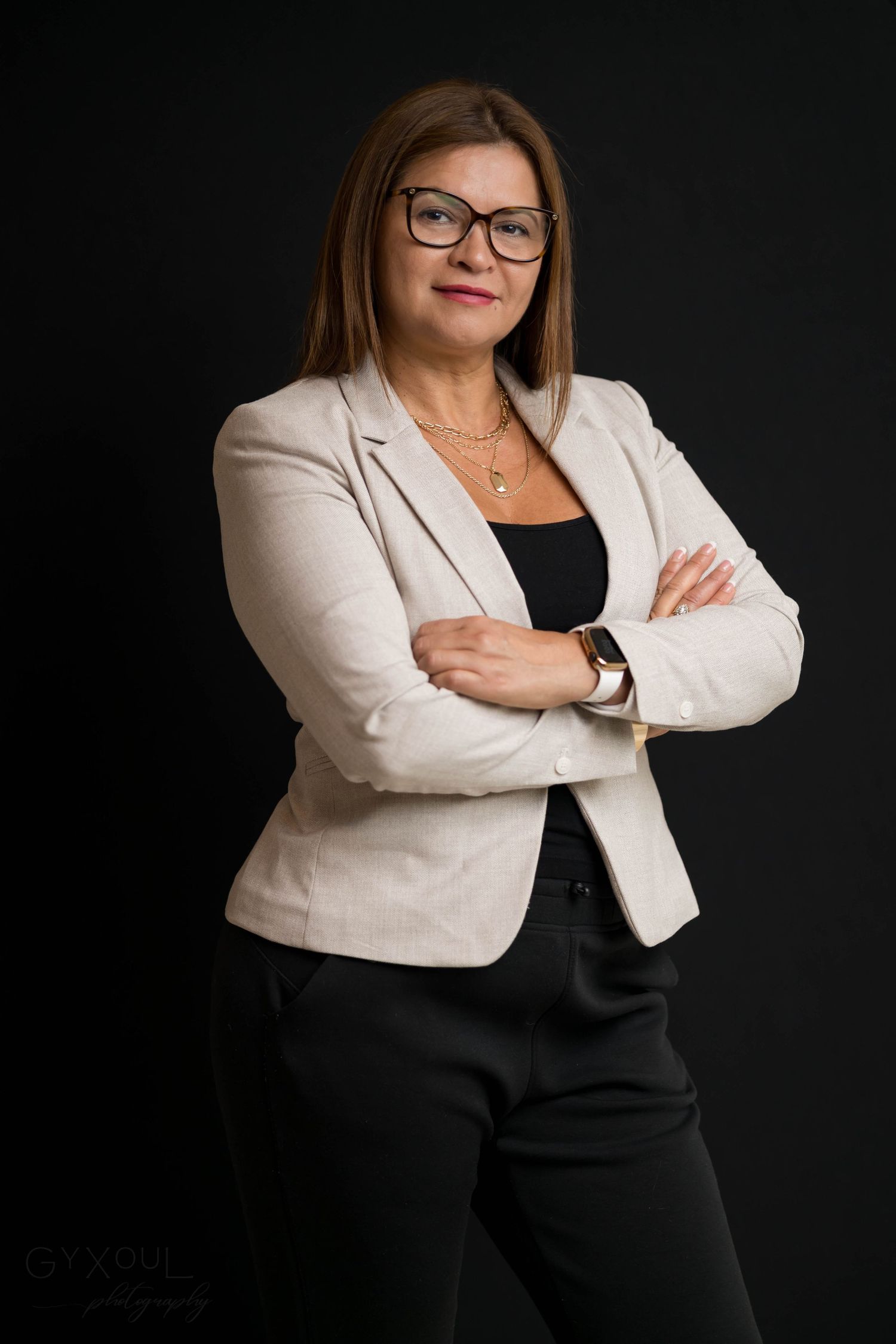 Professional portrait of someone in a beige blazer and glasses against dark background.