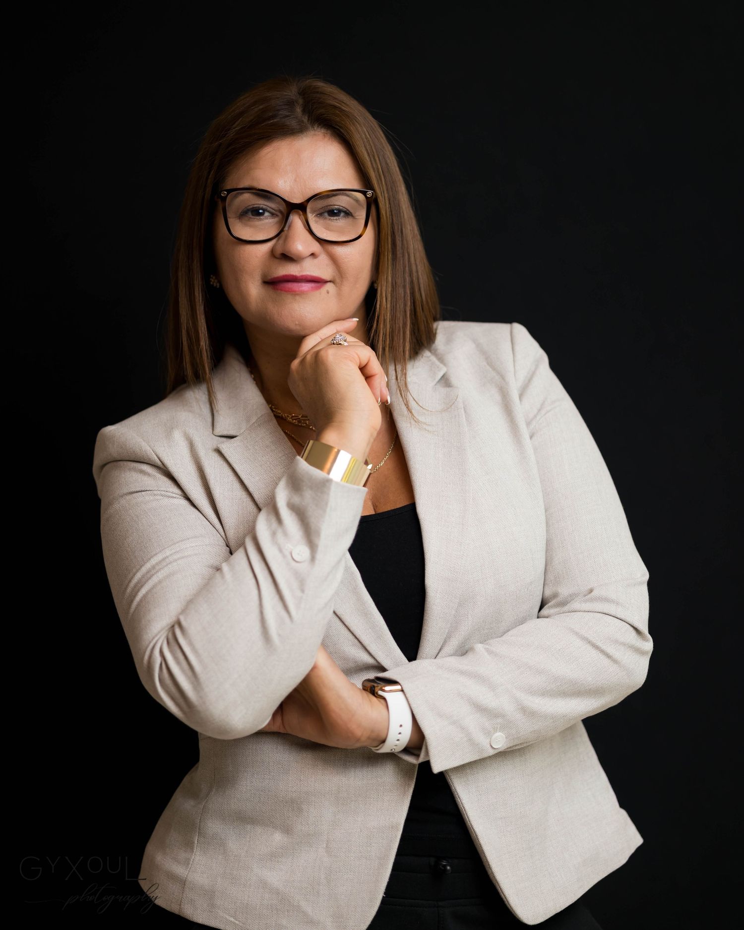Business portrait showing someone in glasses and cream blazer with thoughtful pose.