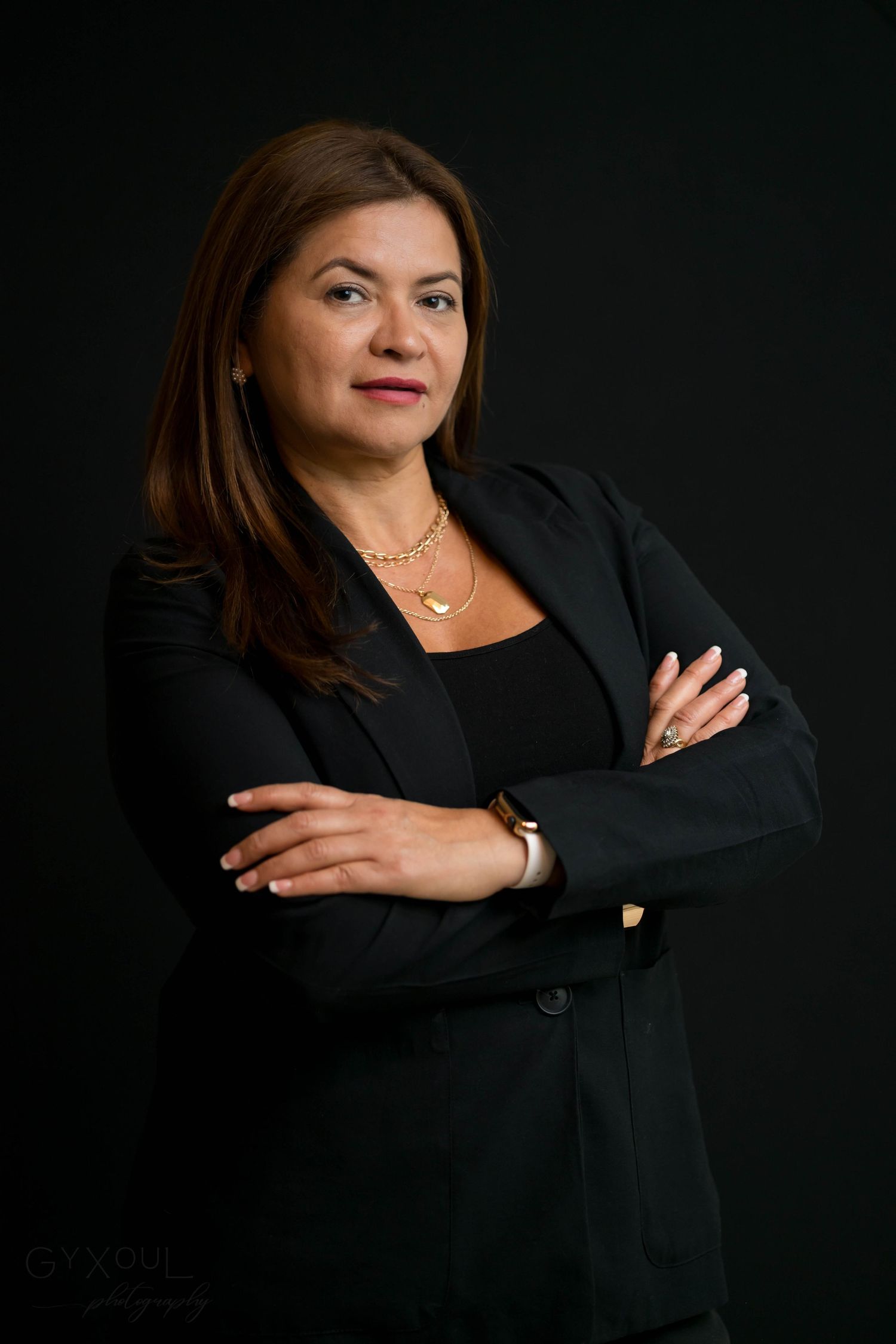 Professional headshot featuring someone in black blazer with crossed arms.