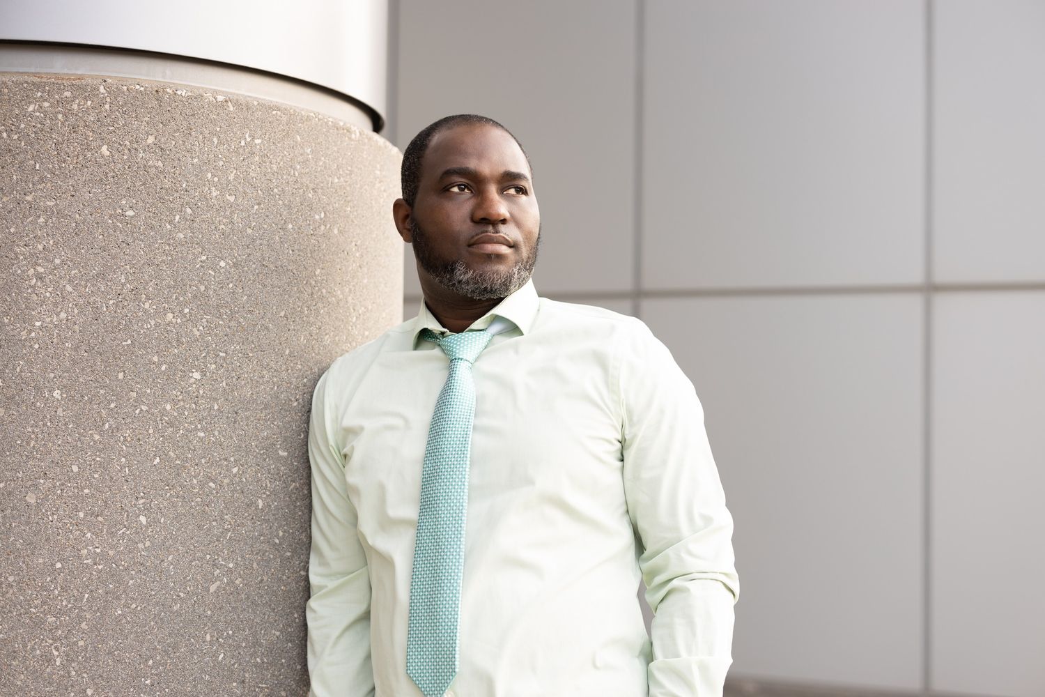 Professional headshot of someone wearing a light dress shirt and tie against a modern building.