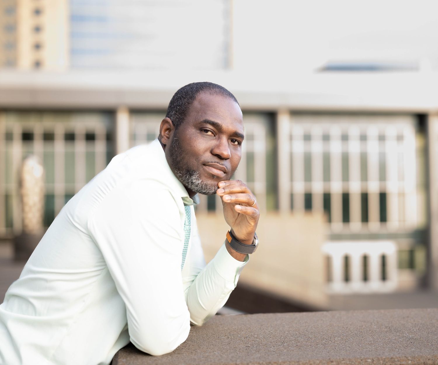 Business casual portrait of someone in a white blazer leaning on a ledge.