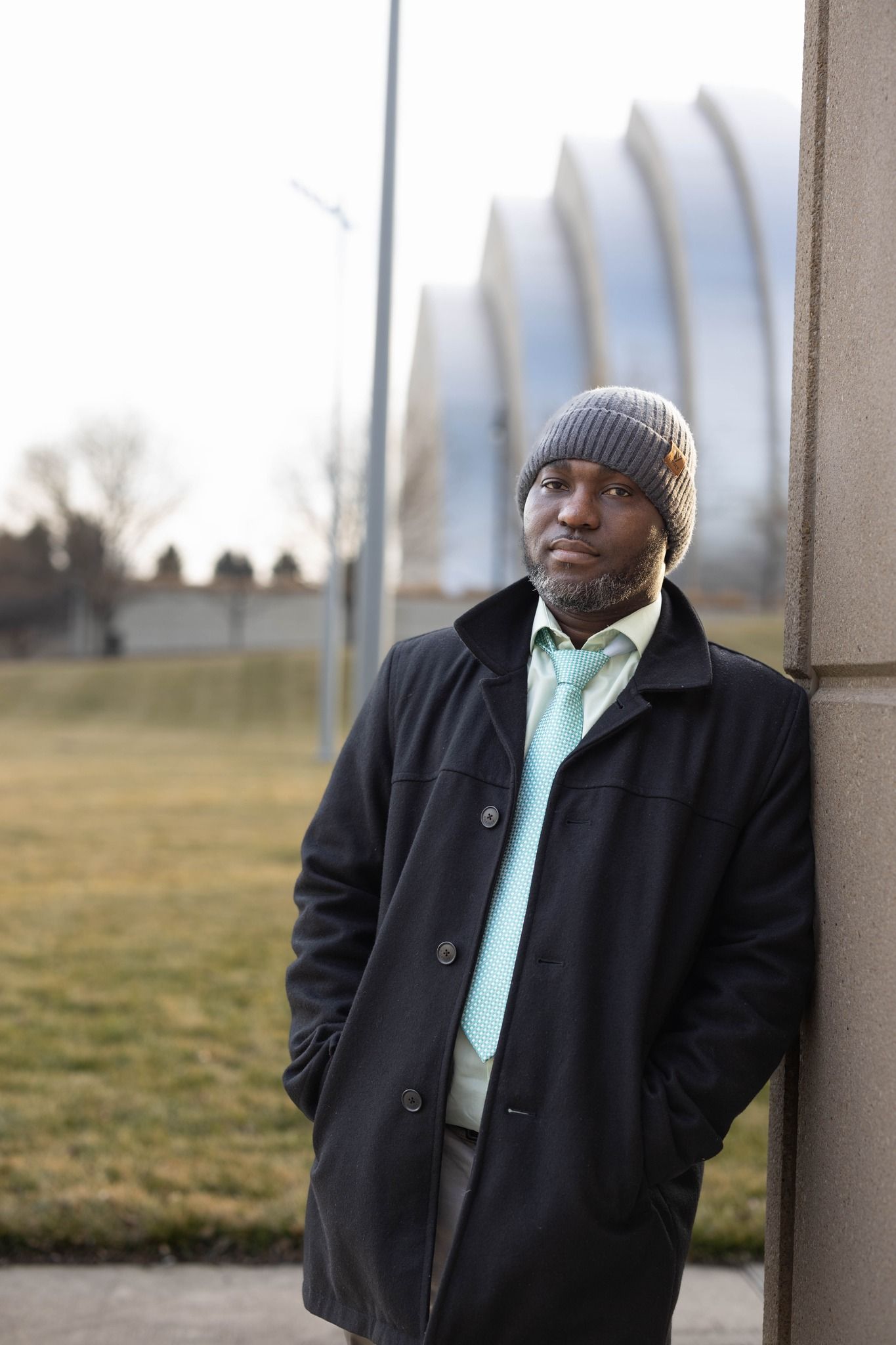 Professional portrait of someone in a winter coat and knit hat standing outdoors.