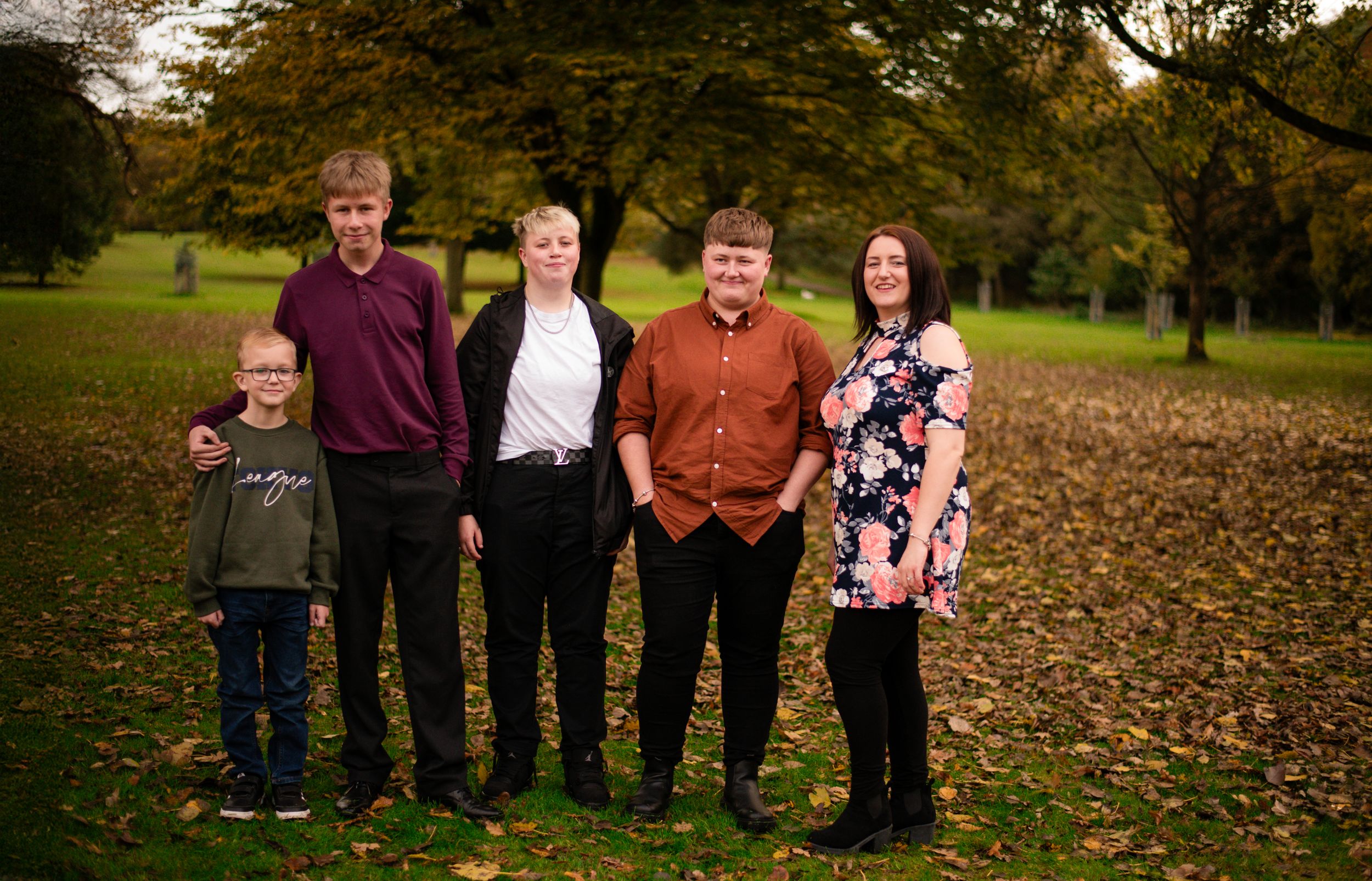 Family portrait taken outdoors in autumn with fallen leaves on the ground.