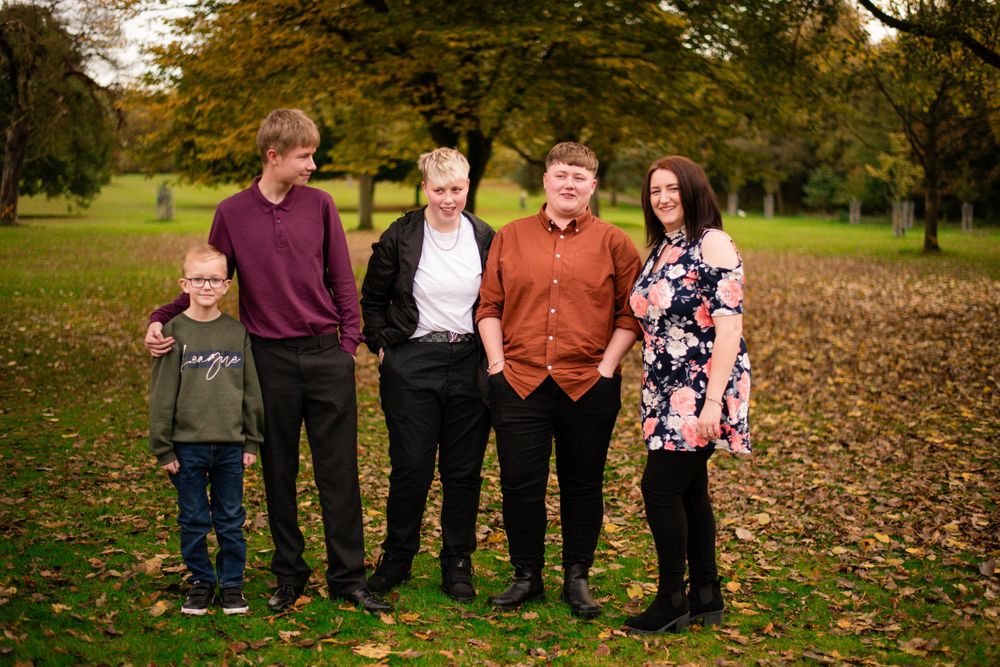 Family group photo in a park setting during fall with colorful foliage in background.