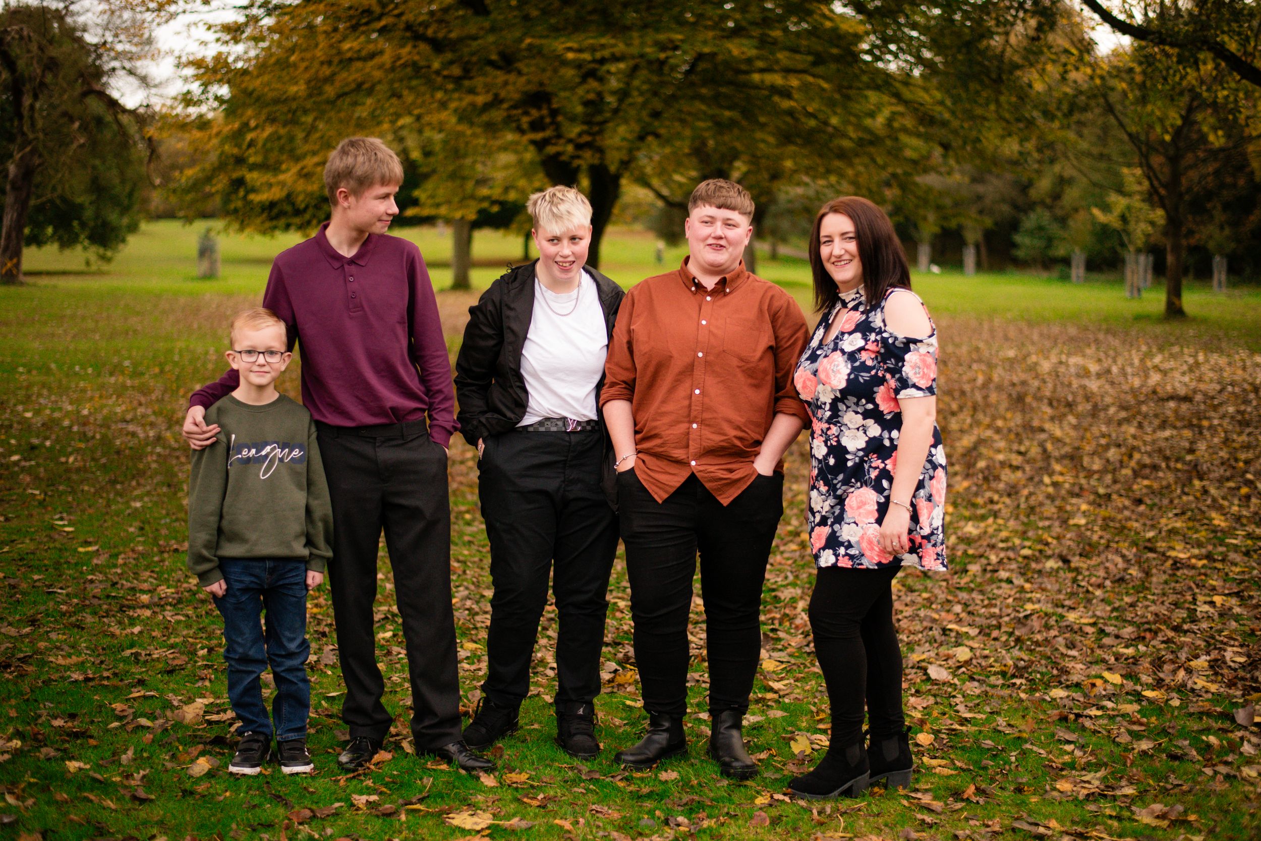 Family group photo in a park setting during fall with colorful foliage in background.