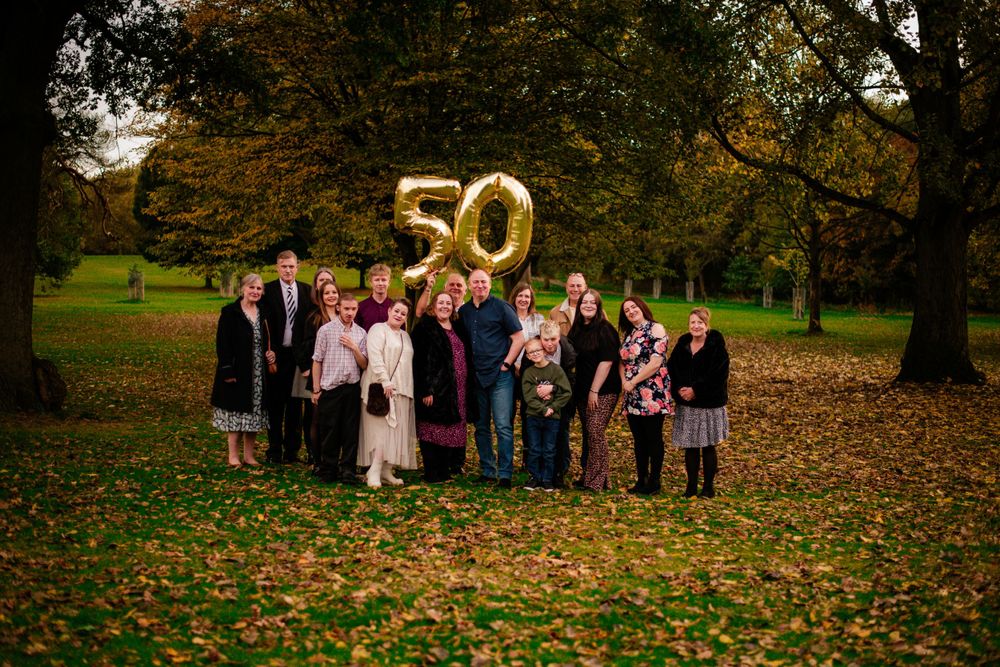 Large family gathering outdoors with gold number 50 balloons celebrating an anniversary.