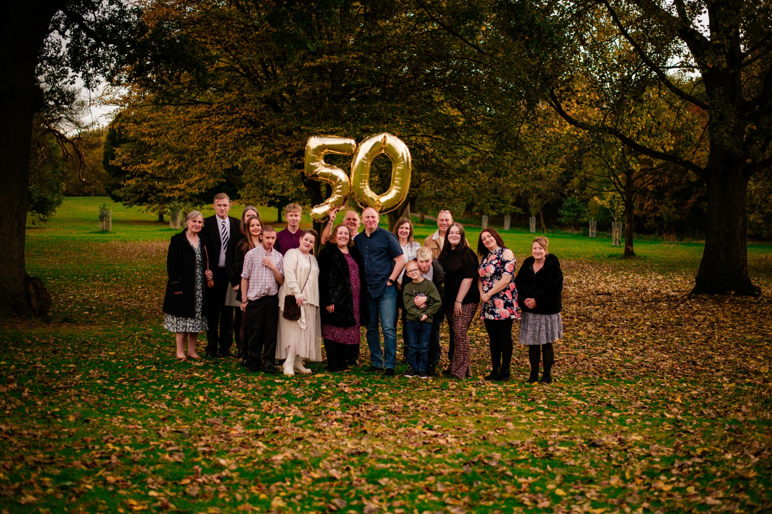 Large family gathering outdoors with gold number 50 balloons celebrating an anniversary.