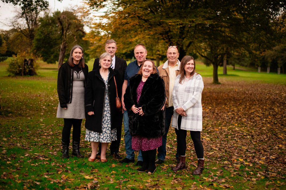 Group photo of family members standing together in a park during fall season.