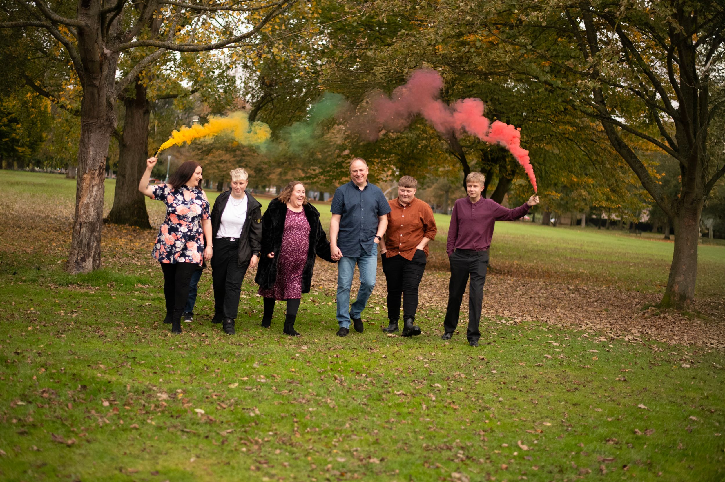 Family members holding colorful smoke flares while walking through autumn park.