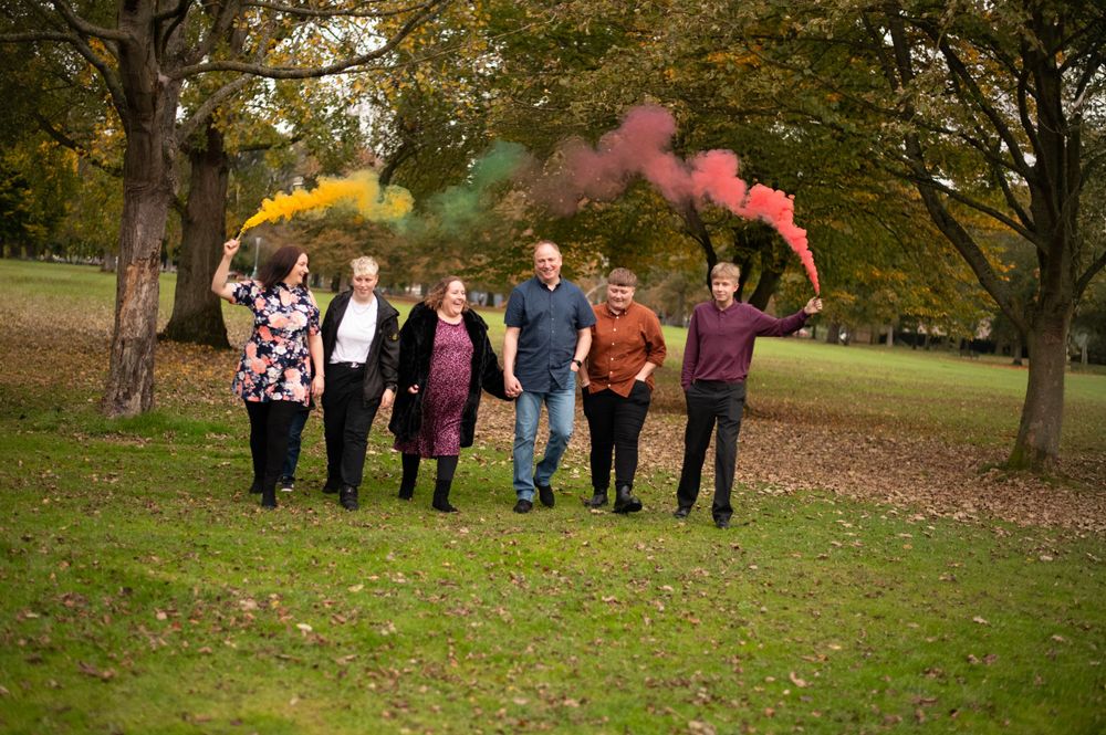 Family members holding colorful smoke flares while walking through autumn park.