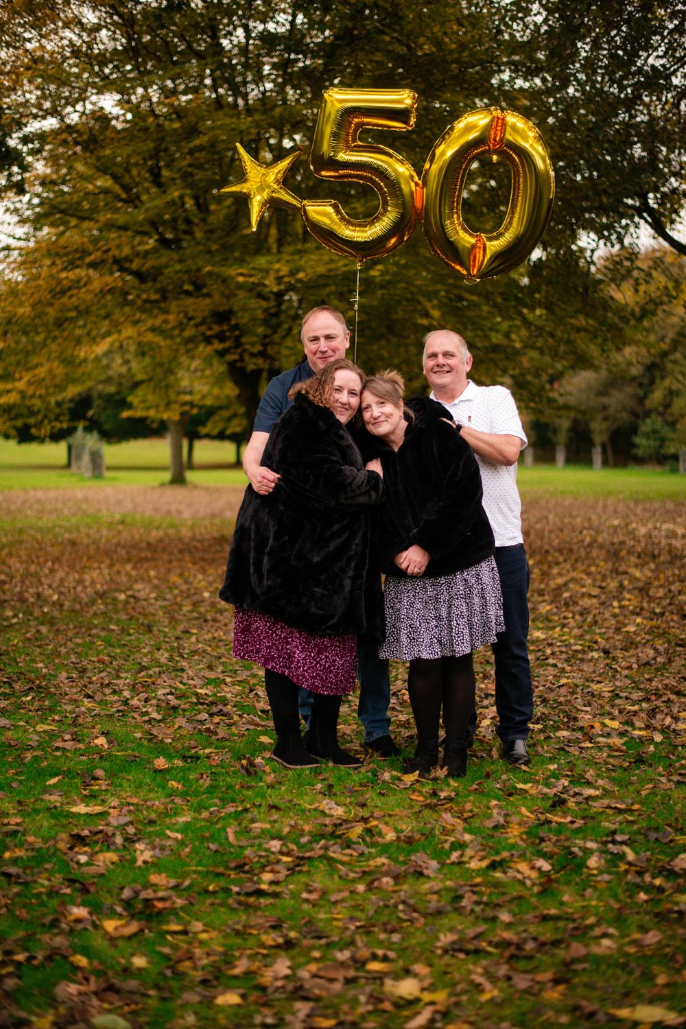 Family photo with golden number 50 balloon decorations in autumn park setting.