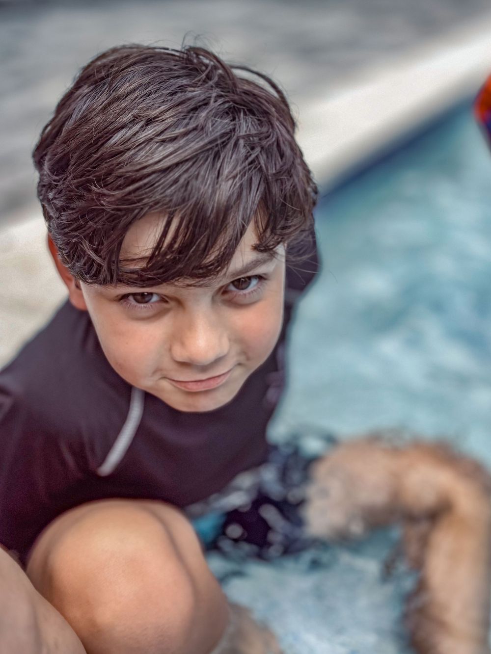 A person in a black wetsuit by a pool on a sunny day.