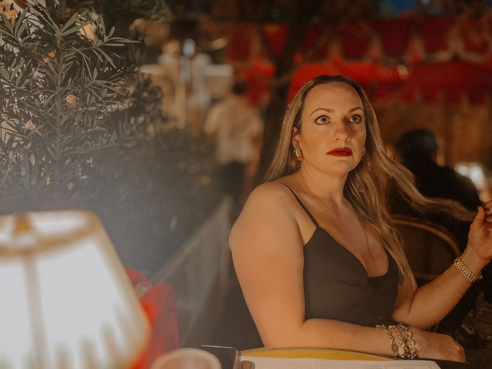 A woman with long blonde hair sitting at a dimly lit restaurant table.
