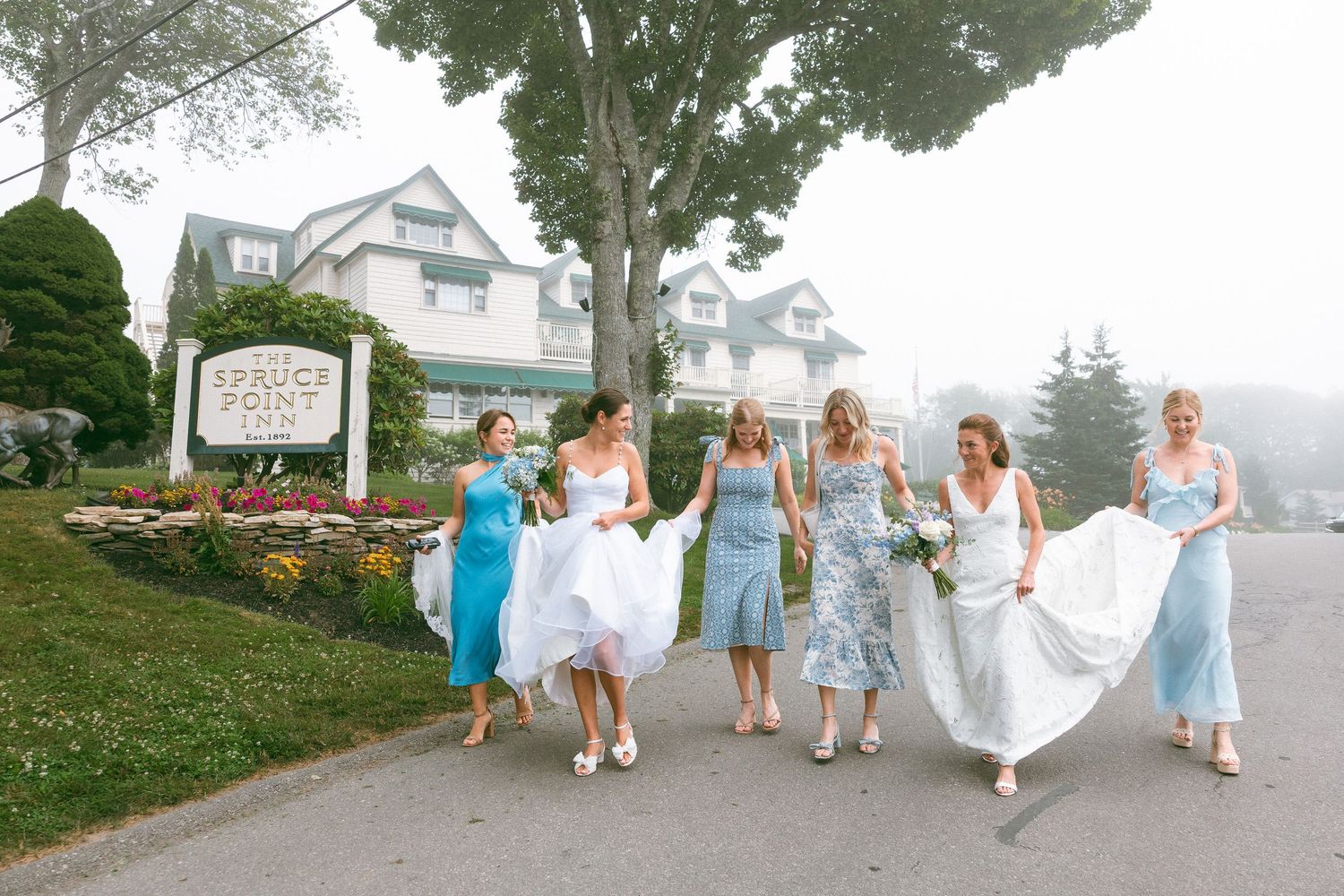 Bridal party in light blue dresses walking together on a grassy hillside.