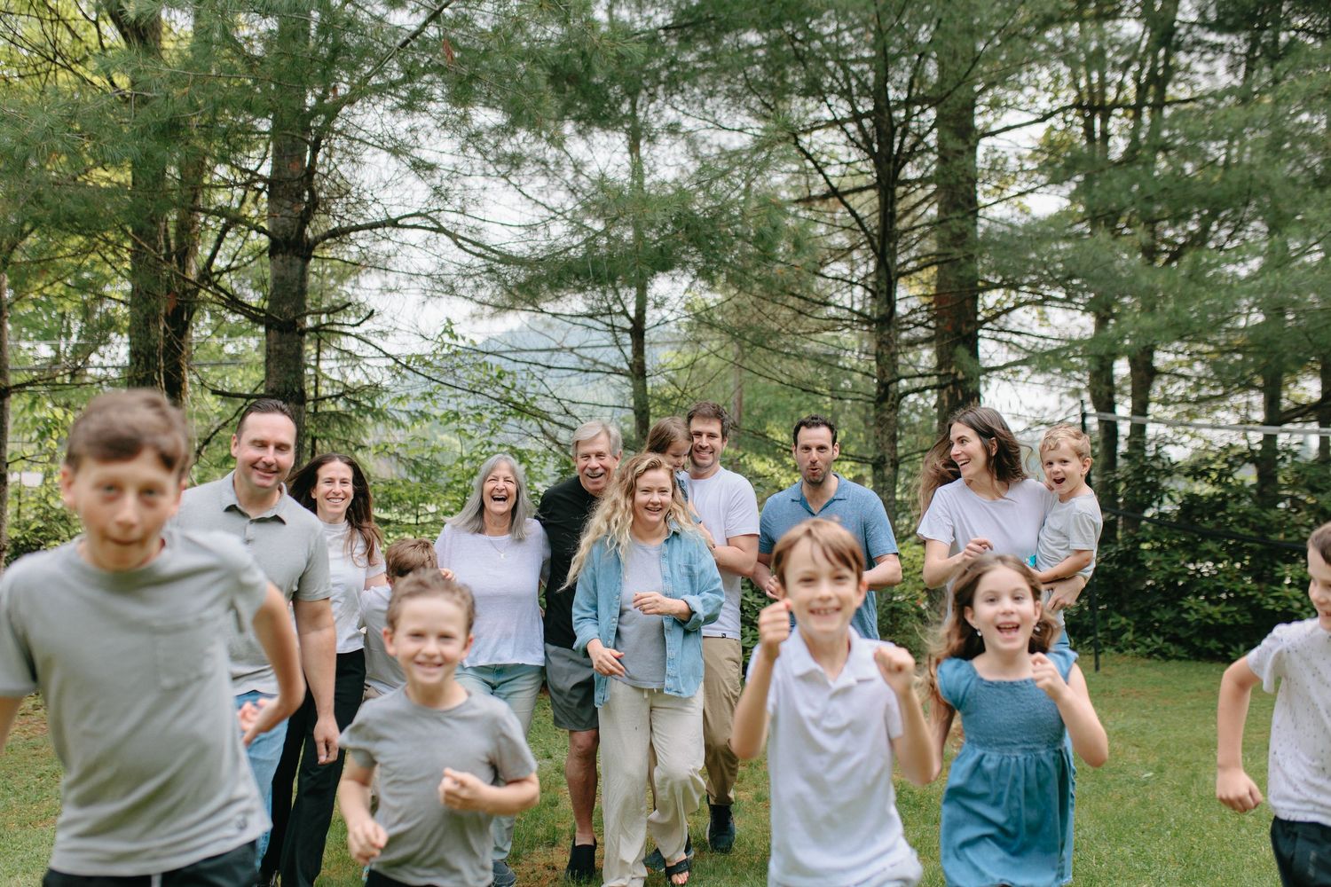 A cheerful group gathered outdoors in a lush pine forest setting on a bright summer day.