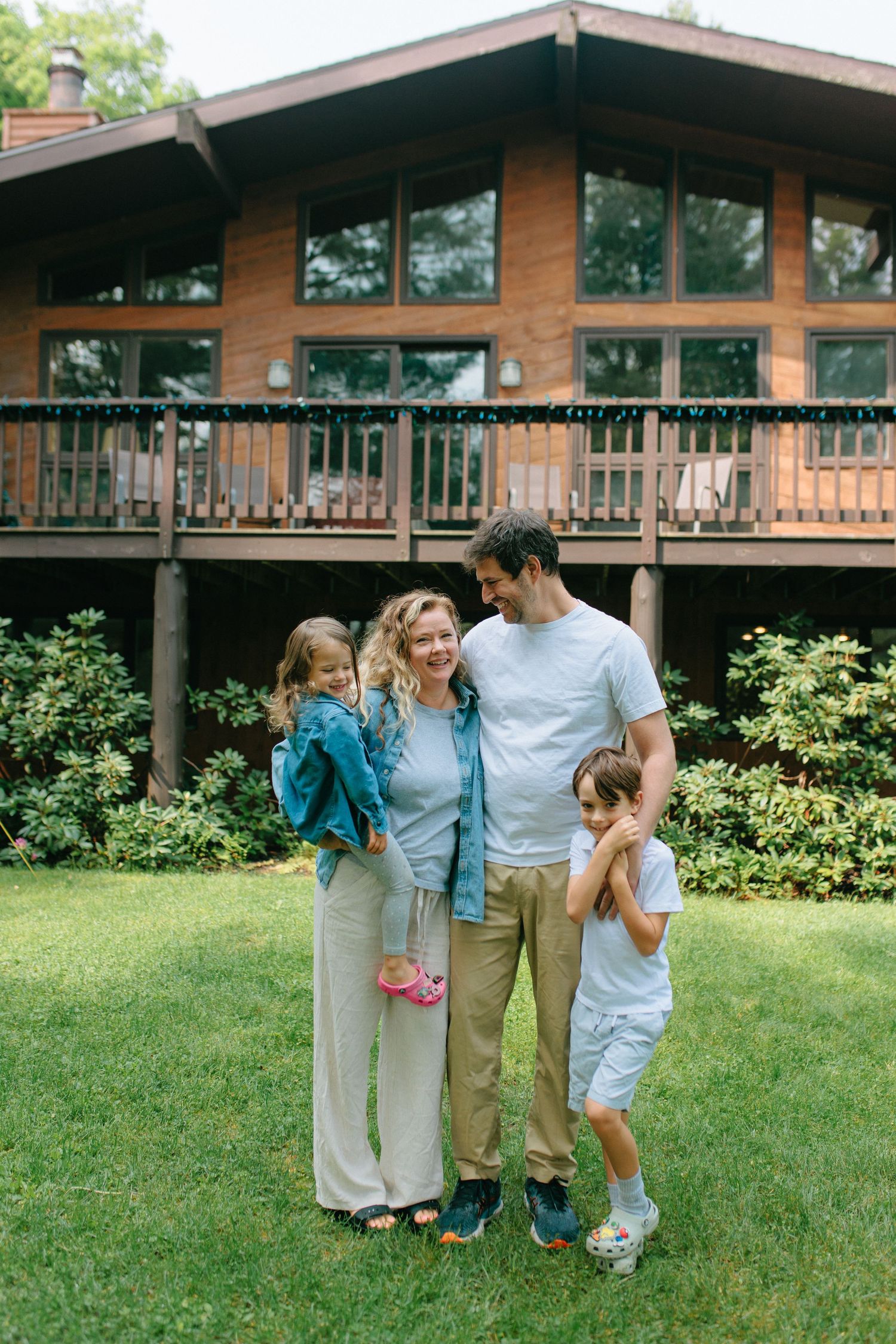 A group of people stand together in front of a wooden lodge building on a grassy lawn during a sunny day.