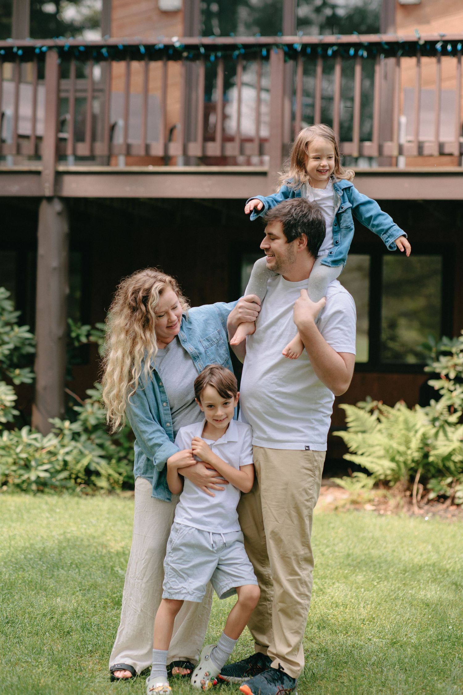 Family wearing matching blue and neutral tones enjoying time together in a backyard with a deck in the background.
