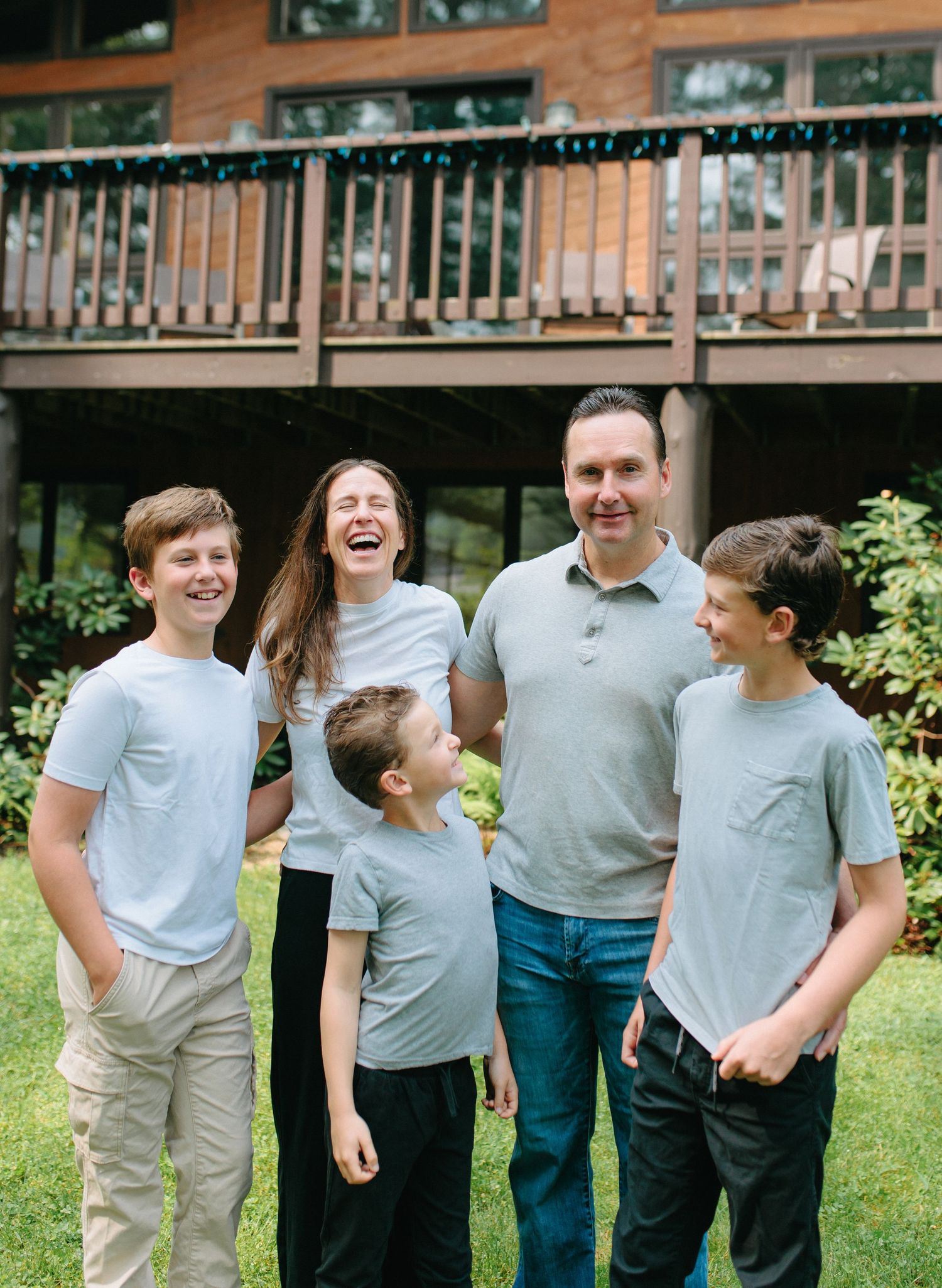 A family of five shares a candid moment of laughter together in front of their brown deck on a sunny day.