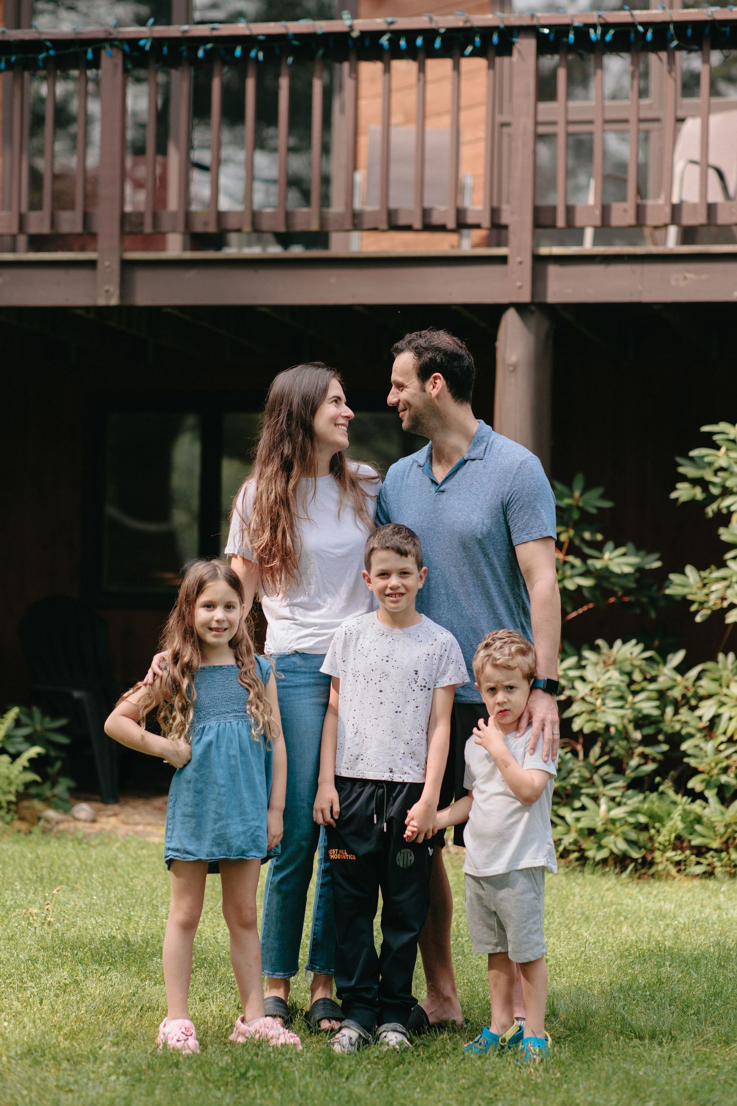 Group stands together on grass in backyard with wood deck and greenery in background.