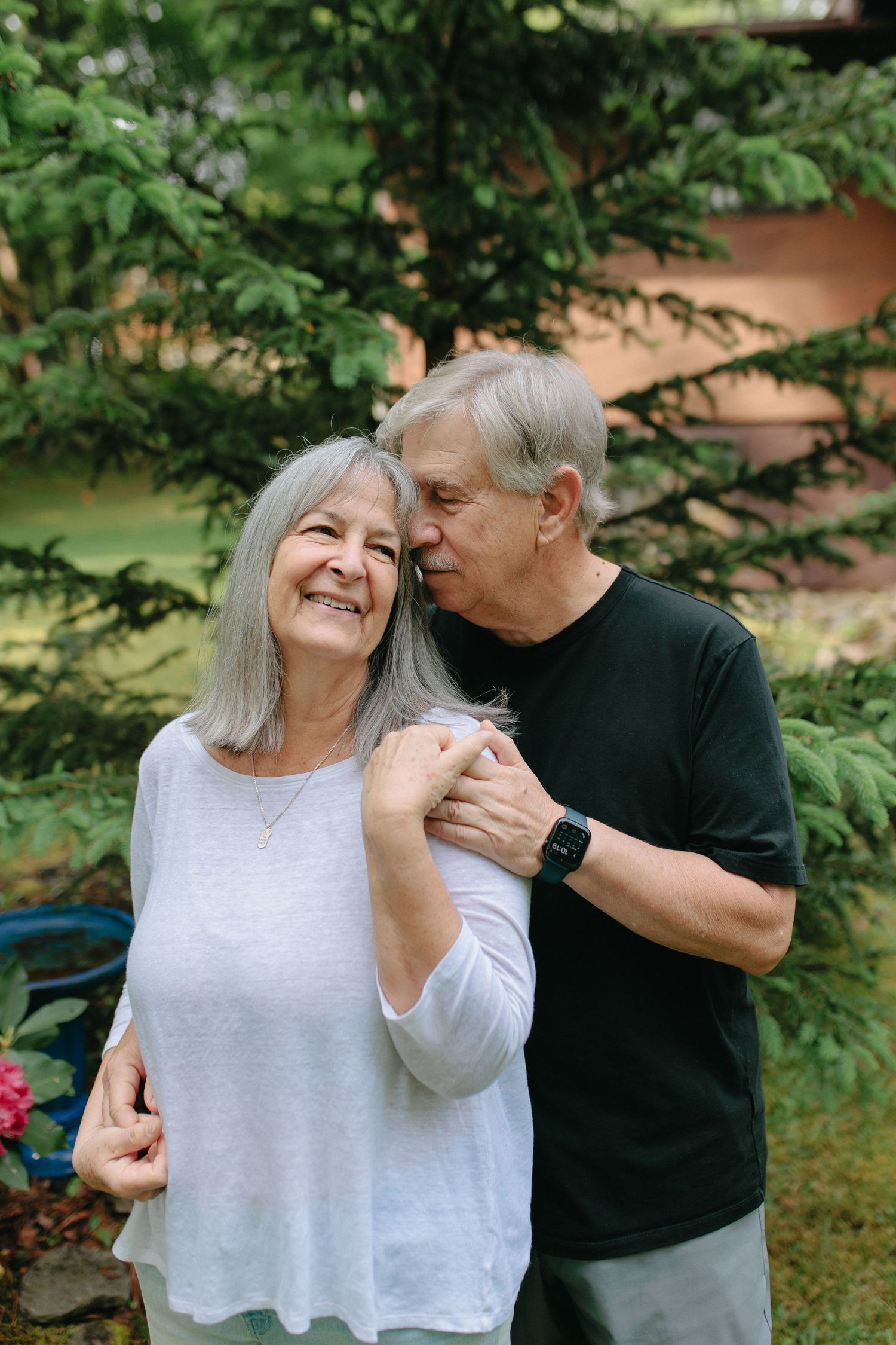 A mature couple sharing an intimate moment together in a garden setting with green foliage in the background.